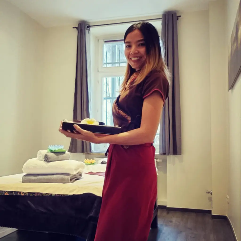 Thai Masseurin mit willkommender Geste im Massagezimmer von Sila Spa München.