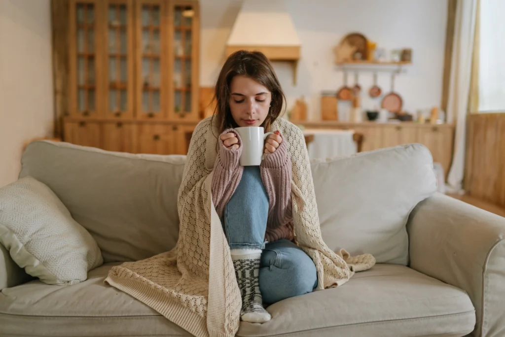 Junge Frau wärmt sich auf dem Sofa mit einer Tasse Tee. 