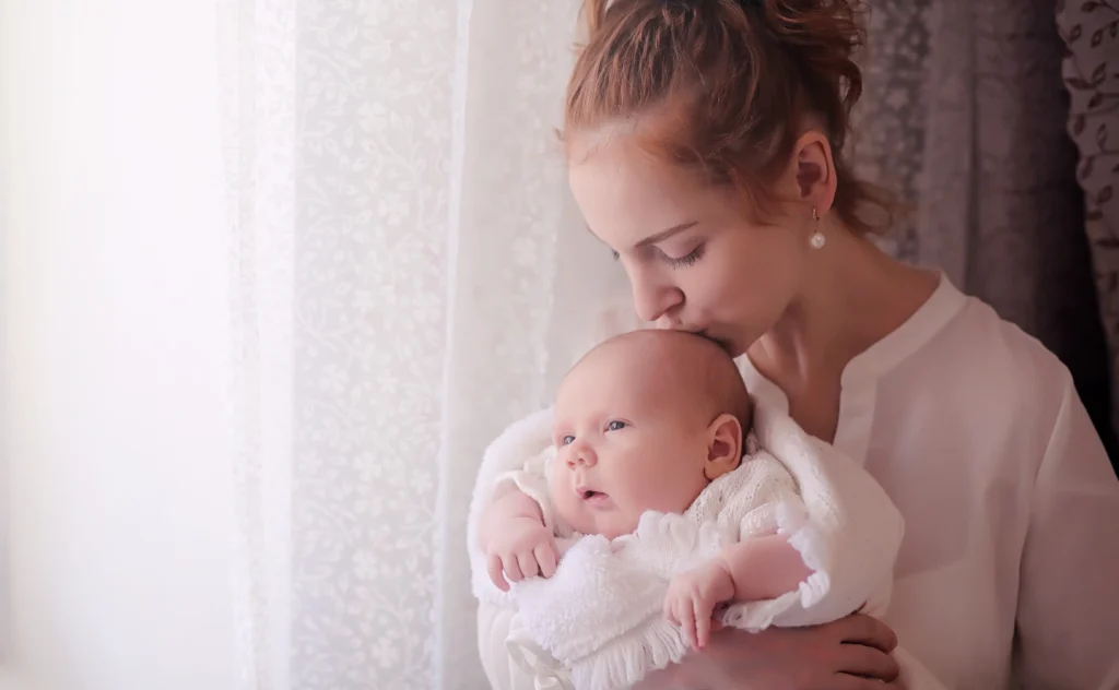 Mutter mit Neugeborenem auf dem Arm, melancholisch am Fenster